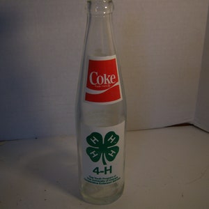 May include: A clear glass Coca-Cola bottle with a red and white label. The bottle has a green 4-H clover logo with the text "The Youth Program of The University of Georgia Cooperative Extension Service" printed below.