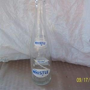 May include: A clear glass bottle with a blue and white label that says "Just Whistle" and "Thirsty?"  The bottle is a vintage soda bottle.