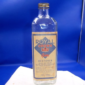 May include: A clear glass bottle with a metal cap, featuring a label that reads "Royal Crown Gem Restorer." The label has a diamond-shaped design with a crown and the words "Clean-Wax-Polish."