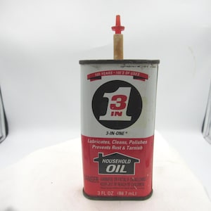 May include: A vintage 3-IN-ONE Household Oil can. The can is primarily white with a red and black label. The label features the text "3 IN ONE" inside a black circle. A red and tan spout is inserted in the top.