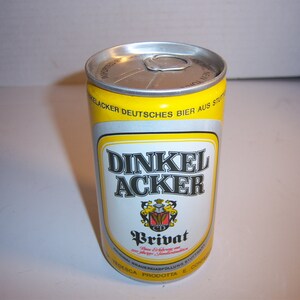 May include: A silver can of Dinkel Acker Privat beer. The can is yellow and white with black text. The text on the can reads "Dinkel Acker Privat" and "Deutsches Bier aus Stuttgart".