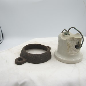 May include: An antique electrical insulator and a rusty metal ring with a loop. The insulator is white with a broken section and wire. The ring is dark brown and circular, with a small loop attached.