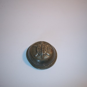 May include: A small, antique-style metal dish with a raised turtle design in the center. The dish has a rounded shape with a decorative, textured edge. The color is a muted, aged silver.