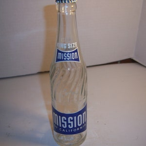 May include: Clear glass Mission soda bottle with a blue and white label. The bottle has a textured, swirled design and a silver cap. The label reads "Mission" and "King Size".
