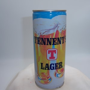 May include: A vintage Tennent's Lager beer can. The can features a blue top, a white and orange design with the words "TENNENT'S LAGER" and a red "T" logo. The can is cylindrical and appears to be made of metal.