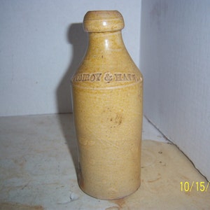May include: A tan ceramic bottle with a rounded top and a label that reads "Tomroy & Hall".