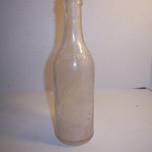 May include: A clear glass bottle with a label that reads "Registered" and "The Original Big 12 oz.  PEPSI-COLA  Bottled by  PEPSI-COLA BOTTLING CO.  OF  DALLAS, TEXAS".