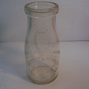 May include: A clear glass milk bottle with a white label that reads "Half Pint - 1/2 Ounces - D. Bassett & Prentice -  Brewster, N.Y."