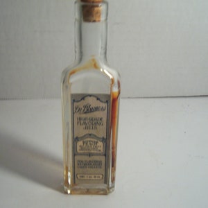 May include: A small, clear glass bottle with a cork stopper. The bottle contains a brown liquid and has a label that reads "Dr. Blumers High Grade Flavoring Jelly" with the text "Nutty Chocolate" in a smaller font.
