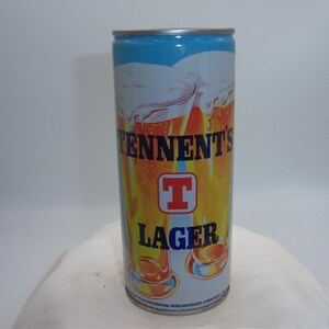 May include: A cylindrical Tennent's Lager beer can. The can features a blue top, with the brand name and "Lager" in bold letters. The design includes images of beer glasses and a red "T" logo.