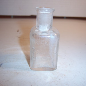 May include: A clear glass bottle with a square body and a round neck. The bottle has a label that reads "Dr. J.H. McLean's" and "St. Louis, Mo."