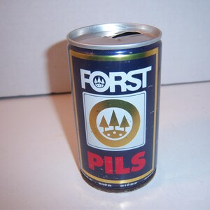 May include: A blue aluminum can with a gold and white label. The label says "FORST" in white letters and "PILS" in red letters. The label also features a gold circle with three stylized trees inside.