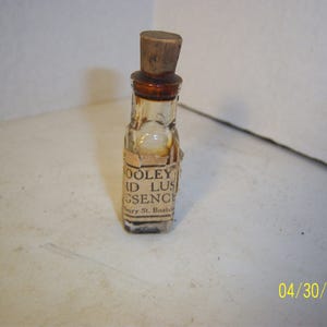 May include: A small, clear glass bottle with a brown cork stopper. The bottle is labeled "Dooley's Liquid Ginseng" and "Henry St. Boston".