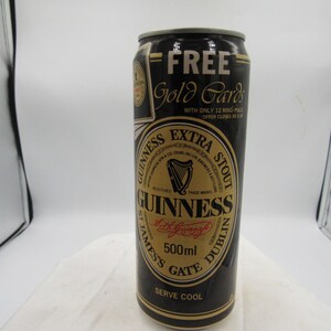 May include: A black Guinness Extra Stout beer can with gold accents. The can features the Guinness logo, a harp, and the text "500ml". The can also has the text "FREE Gold Cards".