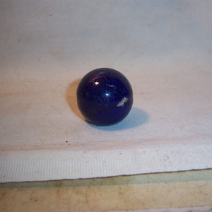 May include: A dark blue glass marble.