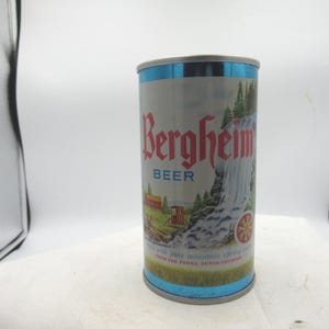 May include: Vintage Bergheim Beer can with a silver body, blue accents, and red lettering. The can features a scenic illustration of a waterfall, trees, and a building. The text "BEER" is below the brand name.