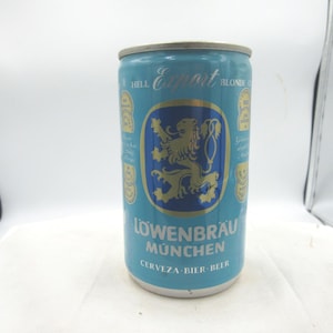May include: A vintage Löwenbräu beer can in light blue with gold and navy blue accents. The can features a lion emblem and the text "Löwenbräu München" and "CERVEZA - BIER - BEER". The can is cylindrical and has a silver top.