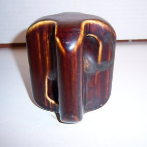 May include: A brown ceramic insulator with a white glaze. The insulator has a hole in the center and two holes on the sides.