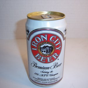 May include: A white aluminum can of Iron City Beer. The can has a red and white logo with the words "Iron City Beer" and "Pittsburgh Brewing Co. Since 1861". The can also has the text "Premium Beer Saluting the 1995 AFC Champions".