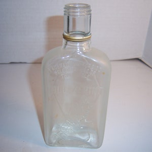 May include: A clear glass bottle with a gold top. The bottle has the words "Pendleton Sale" and "Original Wine of the West" embossed on the front.