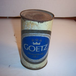 May include: A vintage, rusty, aluminum can of Goetz Premium Quality Beer. The can is white with a blue and gold label featuring a crown and the brand name.
