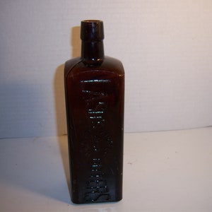 May include: A dark brown glass bottle with a square shape and a label that reads "Dr. J.H. McLean's" and "Liver & Kidney Balsam".