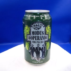 May include: A green aluminum can of Modus Hoperandi India Pale Ale. The can features a logo with the text "SKA Brewing" and a graphic of three men in suits. The can also has the text "12 fluid oz (355 ml)".