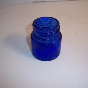 May include: A small, cobalt blue glass jar with a rounded shape and a wide mouth.