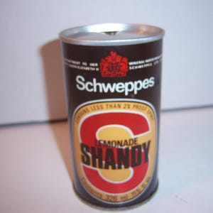 May include: A brown aluminum can with a white and red label. The label says "Schweppes Lemonade Shandy" and features a large letter "S".
