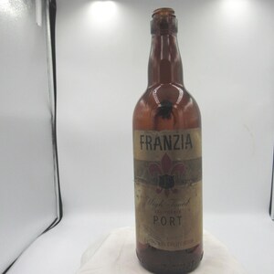 May include: A vintage brown glass bottle with a label that reads "Franzia" and "Port". The label has a floral design and the words "High Tower California". The bottle is empty and has a long neck.