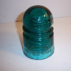 May include: A teal blue glass insulator with a rounded top and a wide base. The base is marked with the text "D.C.T. 522 1507."