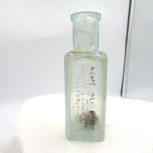 May include: A clear, rectangular glass bottle with a narrow neck. The bottle has text that reads "AGME ALAKING" and "TRADE MARK WOLFF & RANDOLPH PHILADELPHIA". The bottle is empty and has a slightly aged appearance.