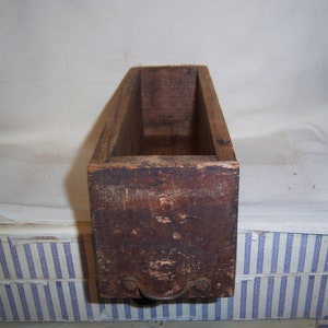 May include: A rectangular, open-top wooden box with a dark brown finish. The box has a handle on the front and shows signs of wear, suggesting it is an antique or vintage item. The wood grain is visible.