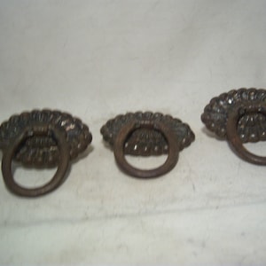 May include: Three antique bronze drawer pulls. Each pull features a decorative, fan-shaped backplate with a circular handle. The hardware has a weathered appearance, suggesting age and use. Ideal for furniture restoration or adding vintage charm.