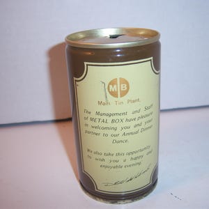 May include: A vintage brown and beige metal can with a gold rim. The can features text that reads "Main Tin Plant" and "METAL BOX" along with an invitation to a dinner dance. The can has a small opening on top.