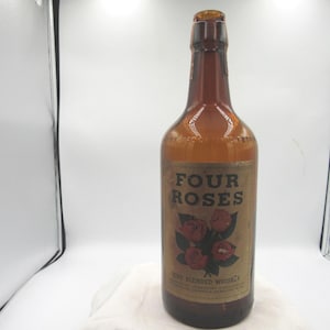 May include: An amber-colored glass bottle of Four Roses blended whiskey. The label features the words "Four Roses" above a graphic of red roses. The bottle is empty and appears to be vintage.