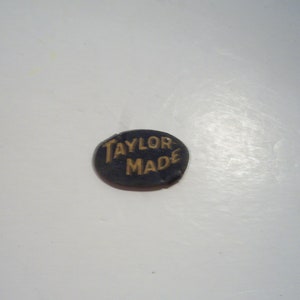 May include: A black oval-shaped tag with the text "Taylor Made" in gold lettering.