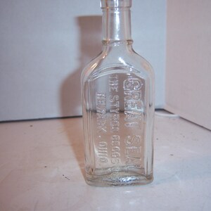 May include: Clear glass bottle with a rectangular label. The label is embossed with the words "GREAT SEAL" and "THE STYER EGG COGS NEWARK, OHIO". The bottle has a rounded shoulder and a narrow neck.