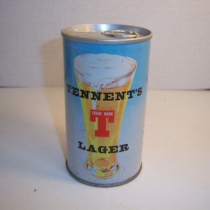 May include: A silver can of Tennent's Lager with a blue background and a glass of beer with a white head. The can has the text "Tennent's" in black letters and "Lager" in black letters below a red "T" with the words "Trade Mark" above it.