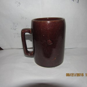 May include: A brown ceramic mug with a handle. The mug has a rustic, aged look.