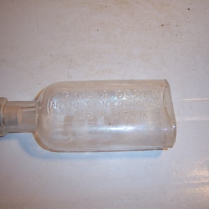 May include: A clear glass bottle with a metal cap. The bottle is labeled "CHAS. M. JOSLIN, NO. 141 WEST 125TH ST. NEW YORK."