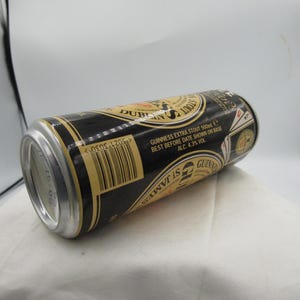 May include: A black and gold Guinness Extra Stout 500ml can, with text including "Dublin" and "St. James". The can has a silver top and base, and the label includes the text "Best Before Date Shown on Base ALC. 4.3% VOL".
