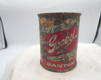 Könnte beinhalten: Vintage Goebel Bantam Bierdose. Die zylindrische Dose hat eine verrostete Außenseite. Ein rot-weißes Etikett trägt die Aufschrift "Light Lager", "Goebel" und "Luxury Beer". Ein antikes Sammlerstück.
