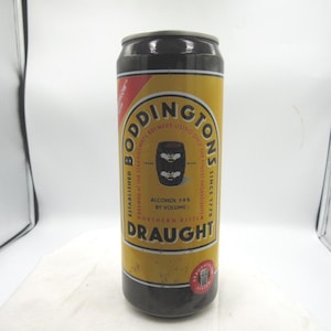 May include: A Boddingtons Draught beer can. The can is yellow with black accents and features the Boddingtons logo and text. The can also states the alcohol content is 3.8% by volume.