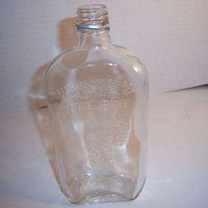 May include: Clear glass bottle with a rounded rectangular shape. The bottle has a narrow neck and a slightly textured surface. The words "FEDERAL LAW FORBIDS SALE OR REUSE OF THIS BOTTLE FULL PINT" are embossed on the front. The word "Malley" is also embossed.