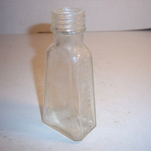 May include: A clear glass bottle with a textured surface and a screw-on lid. The bottle is empty and appears to be vintage.