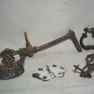 May include: An assortment of antique hardware components, including a silver-toned ornate handle, a brass and twisted metal handle, a decorative ring pull, a small hinge, and a decorative metal piece. The hardware has a vintage aesthetic.