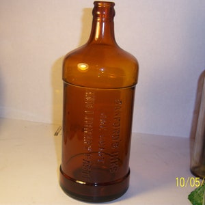 May include: A brown glass bottle with the text "SANFORD'S INK FLUID & INK FOR ALL PENS" embossed on the side.