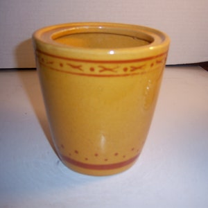 May include: A yellow ceramic jar with a brown rim and decorative brown lines. The jar has a lid.
