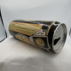 May include: A black Guinness beer can with gold accents and text. The can features a playing card design and the Guinness logo. The can is lying on its side, with the top partially visible.